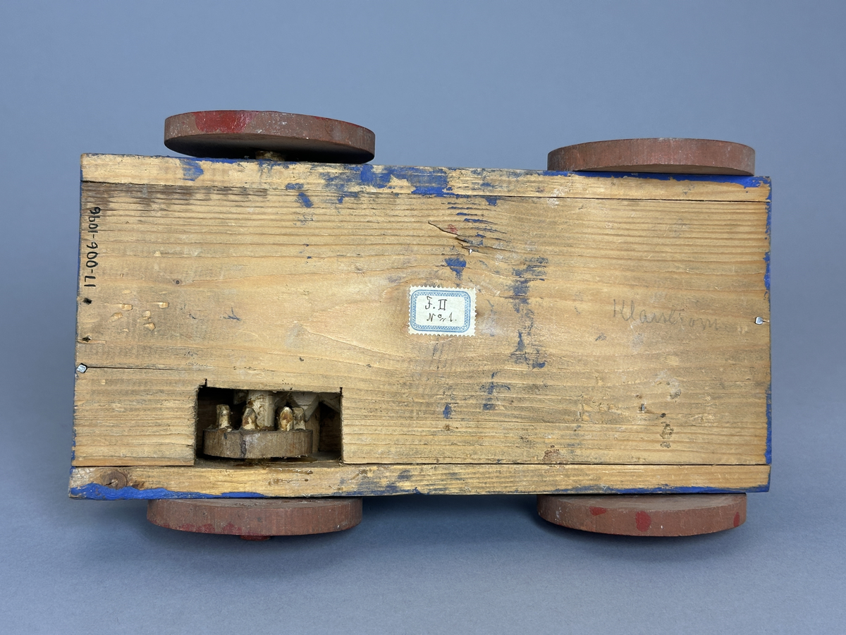 En blå kärra med röda hjul och grön dansbana med tre dansande par. Innuti ett "maskineri", som gör att banan snurras då kärran rullas.