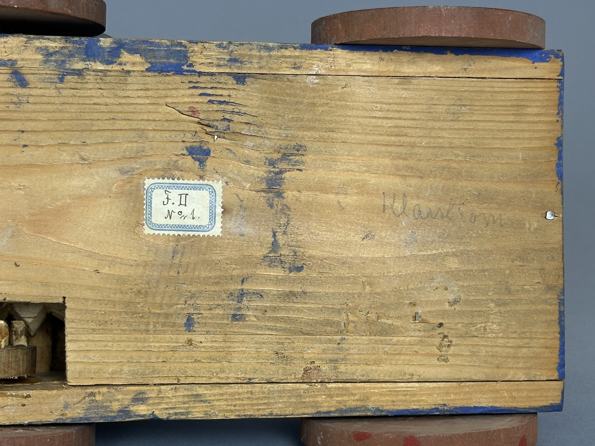 En blå kärra med röda hjul och grön dansbana med tre dansande par. Innuti ett "maskineri", som gör att banan snurras då kärran rullas.