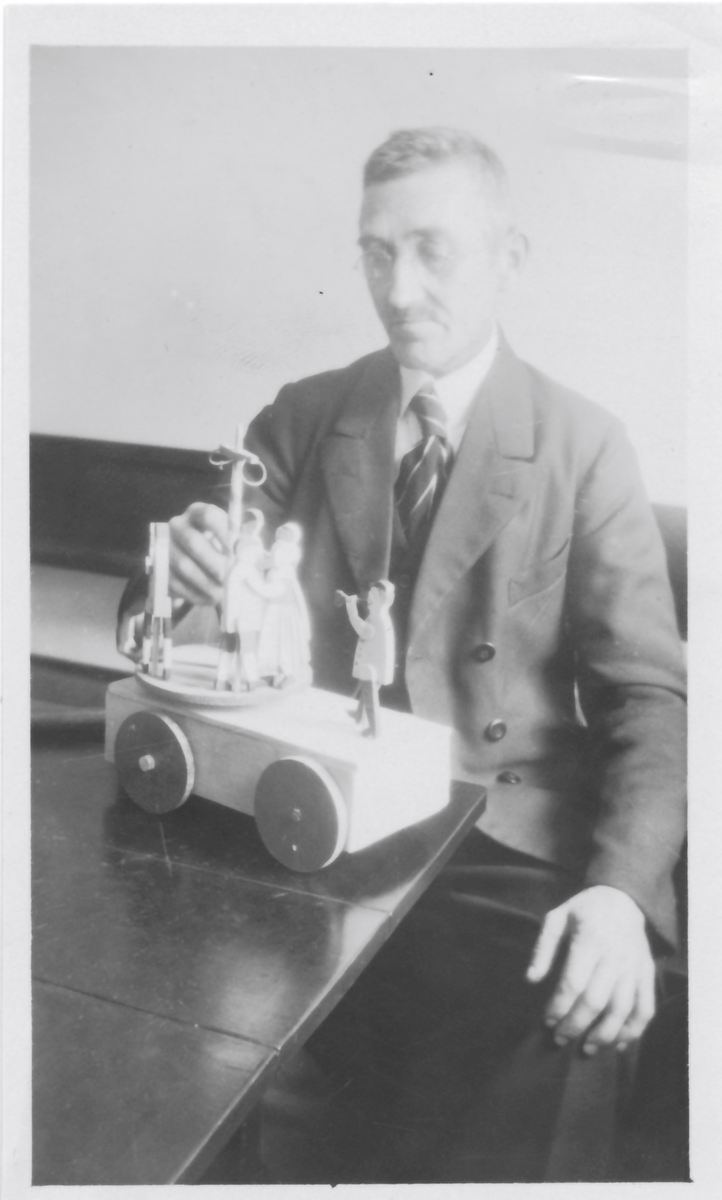 En blå kärra med röda hjul och grön dansbana med tre dansande par. Innuti ett "maskineri", som gör att banan snurras då kärran rullas.