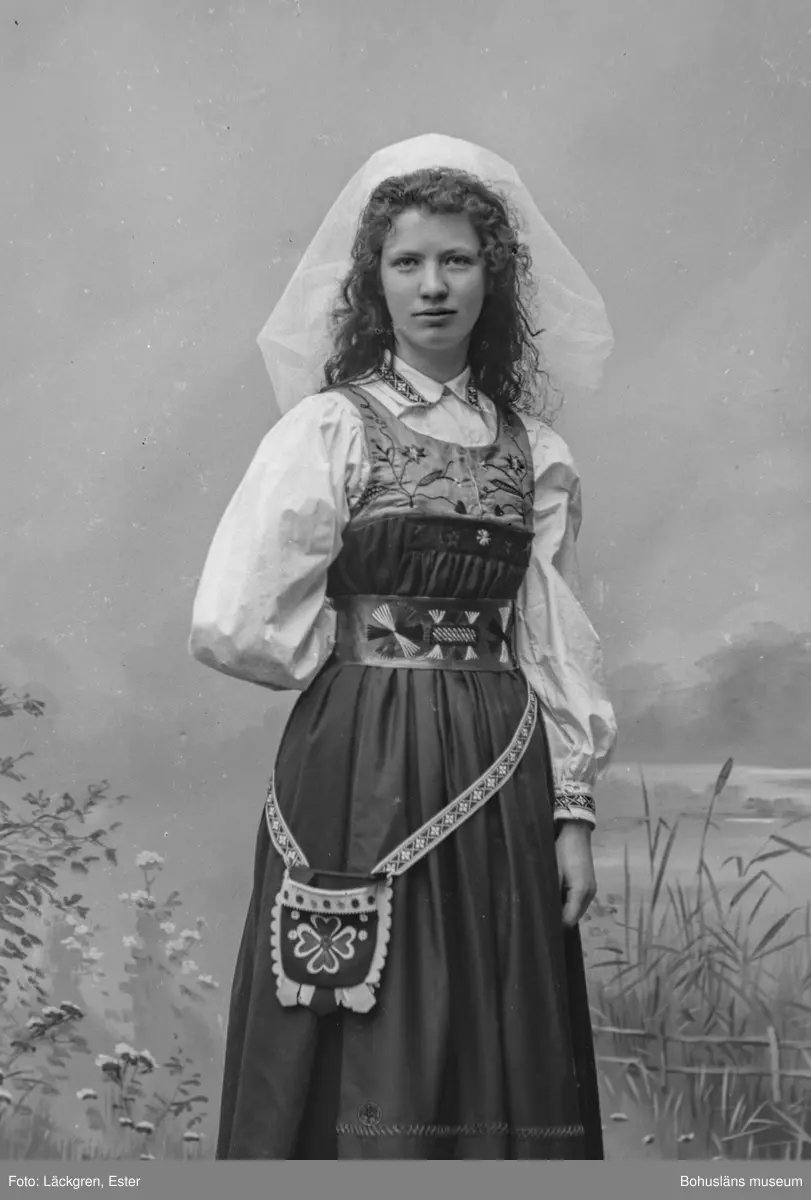 Porträtt av fotograf Ester Läckgren i folkdräkt. 
Text på baksida: Ester