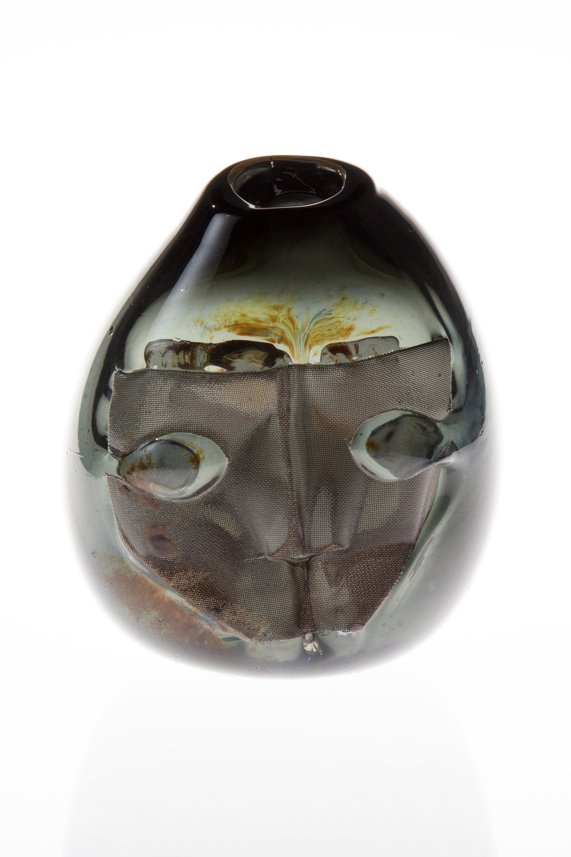 Vase med tilnærmet rund form. Rund åpning på en side i øvre del. Vasen har ilagte metallnett på to sider utformet som to ansikt