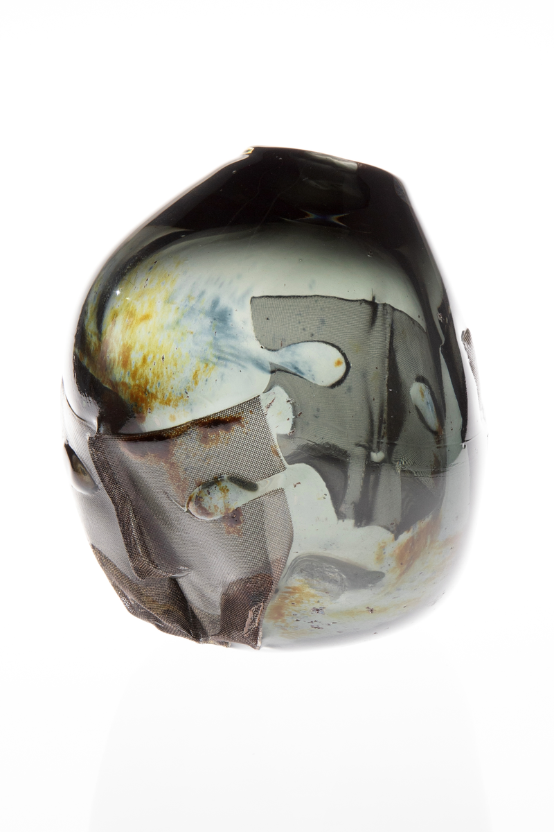 Vase med tilnærmet rund form. Rund åpning på en side i øvre del. Vasen har ilagte metallnett på to sider utformet som to ansikt