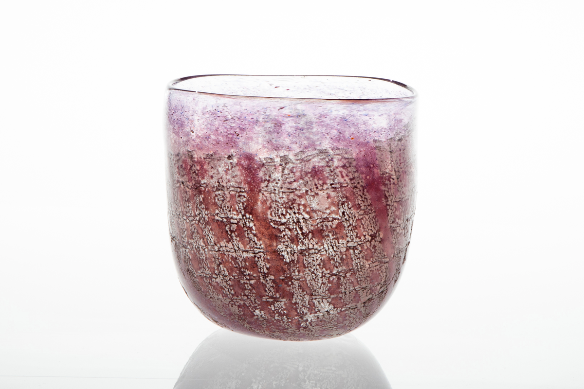 Tilnærmet sylindrisk bolle i halvgjennomskinnelig glass. Overflaten er dekorert med lilla og rødlig emaljefarge samt glassfiber, som danner et rutemønster på bollens nedre del.