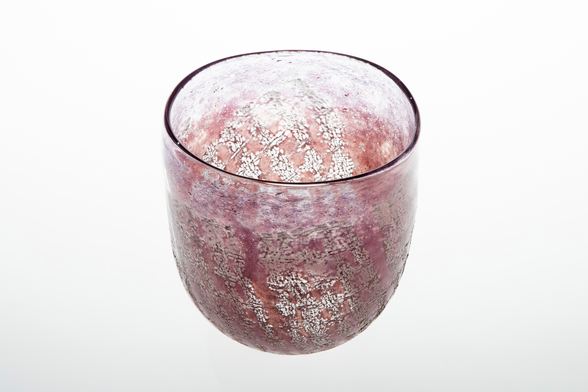 Tilnærmet sylindrisk bolle i halvgjennomskinnelig glass. Overflaten er dekorert med lilla og rødlig emaljefarge samt glassfiber, som danner et rutemønster på bollens nedre del.