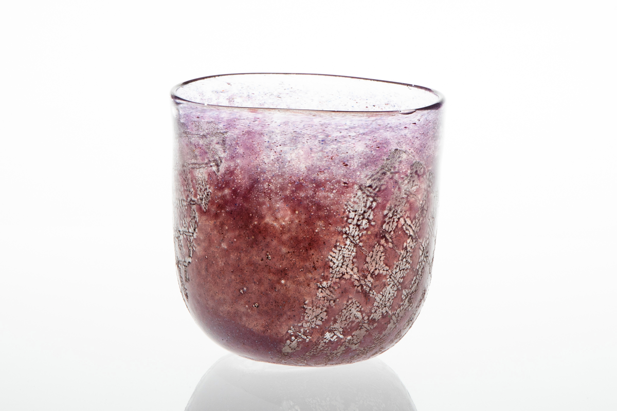 Tilnærmet sylindrisk bolle i halvgjennomskinnelig glass. Overflaten er dekorert med lilla og rødlig emaljefarge samt glassfiber, som danner et rutemønster på bollens nedre del.