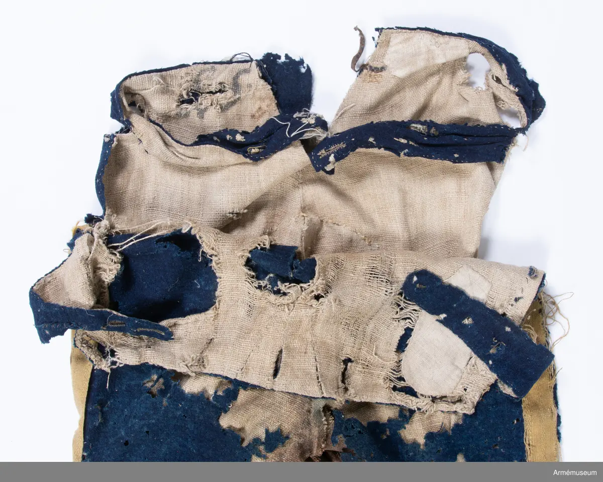 Blå ridbyxor med gula revärer och skinnskodda ben och byxbak.

Byxorna är sydda av ett ganska tunt blått kommisskläde, och är helfodrade med oblekt linne- eller hampalärft.
Modellen är konstruerad med två fram- och två bakstycken, och har hel lucka fram som har knäppts mot en gördel eller linning. Luckan har 5 knapphål fram, varav tre har knäppts mot gördeln. I luckans sidor upptill sitter två spänntampar för knäppning bak i ryggslutet. I sömmen bak sitter en infälld kil för reglering av midjevidden, samt en hank av läder för upphängning.
I sidan har byxorna revärar av 4 cm breda gula redgarnsband.
Byxbenen är skodda med brunt skinn i en höjd av ca 36 cm nertill. Kanten är formad i två bågar fram och en spets bak. Skinnskoningen fortsätter på baksidan upp på insidan av låren och i byxbaken.
Byxorna är mycket trasiga och malätna, och både yttertyg och foder har lagats ett flertal gånger under deras användningstid.
Samtliga knappar saknas förutom i höger byxben längst ner där det sitter rester av enkla skinnknappar i varje sida.

Märkt på insidan "LS No 2".