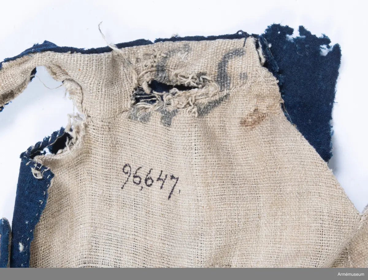 Blå ridbyxor med gula revärer och skinnskodda ben och byxbak.

Byxorna är sydda av ett ganska tunt blått kommisskläde, och är helfodrade med oblekt linne- eller hampalärft.
Modellen är konstruerad med två fram- och två bakstycken, och har hel lucka fram som har knäppts mot en gördel eller linning. Luckan har 5 knapphål fram, varav tre har knäppts mot gördeln. I luckans sidor upptill sitter två spänntampar för knäppning bak i ryggslutet. I sömmen bak sitter en infälld kil för reglering av midjevidden, samt en hank av läder för upphängning.
I sidan har byxorna revärar av 4 cm breda gula redgarnsband.
Byxbenen är skodda med brunt skinn i en höjd av ca 36 cm nertill. Kanten är formad i två bågar fram och en spets bak. Skinnskoningen fortsätter på baksidan upp på insidan av låren och i byxbaken.
Byxorna är mycket trasiga och malätna, och både yttertyg och foder har lagats ett flertal gånger under deras användningstid.
Samtliga knappar saknas förutom i höger byxben längst ner där det sitter rester av enkla skinnknappar i varje sida.

Märkt på insidan "LS No 2".