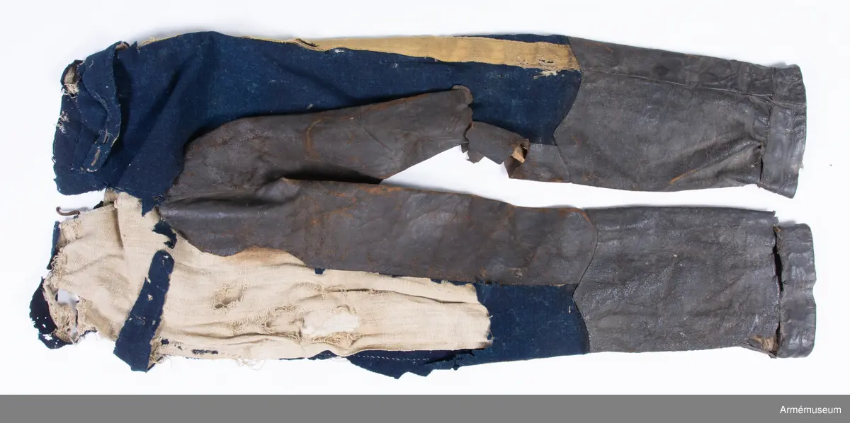 Blå ridbyxor med gula revärer och skinnskodda ben och byxbak.

Byxorna är sydda av ett ganska tunt blått kommisskläde, och är helfodrade med oblekt linne- eller hampalärft.
Modellen är konstruerad med två fram- och två bakstycken, och har hel lucka fram som har knäppts mot en gördel eller linning. Luckan har 5 knapphål fram, varav tre har knäppts mot gördeln. I luckans sidor upptill sitter två spänntampar för knäppning bak i ryggslutet. I sömmen bak sitter en infälld kil för reglering av midjevidden, samt en hank av läder för upphängning.
I sidan har byxorna revärar av 4 cm breda gula redgarnsband.
Byxbenen är skodda med brunt skinn i en höjd av ca 36 cm nertill. Kanten är formad i två bågar fram och en spets bak. Skinnskoningen fortsätter på baksidan upp på insidan av låren och i byxbaken.
Byxorna är mycket trasiga och malätna, och både yttertyg och foder har lagats ett flertal gånger under deras användningstid.
Samtliga knappar saknas förutom i höger byxben längst ner där det sitter rester av enkla skinnknappar i varje sida.

Märkt på insidan "LS No 2".