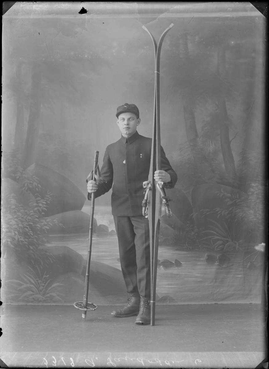 Portrettfotografi. Mann oppstilt i fotostudio kledd i skiklær og med ski og staver i hånden.