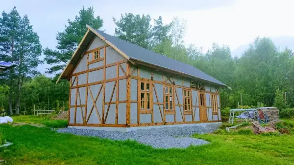 Bilde av et eldhus i bindingsverk i tradisjonell stil. Omringet av skog