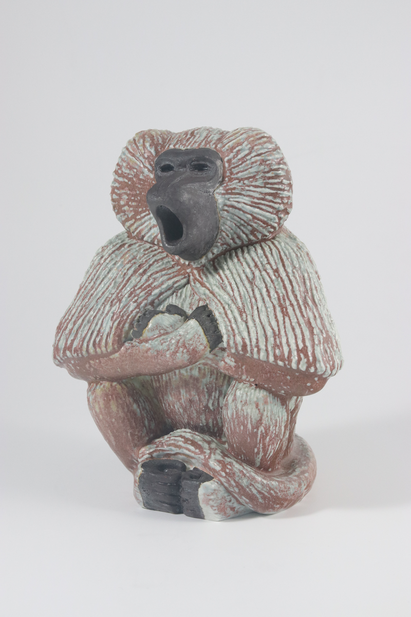 Gunnar Nylund, skulptur, föreställande mantelbabianhane, modellerat stengods med chamotte, blågrön, brun och rödlila glasyr. Rörstrands porslinsfabrik, 1950-talet. Troligtvis prototyp av en senare, numrerad upplaga i vit glasyr.