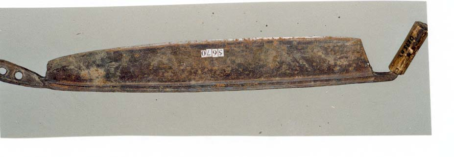 Kniv med breidt jernblad. Handtak av tre i eine enden. Den andre enden av kniven har to hol og skal truleg festast til ein benk e.l. Bladet har ein utydeleg stempel.