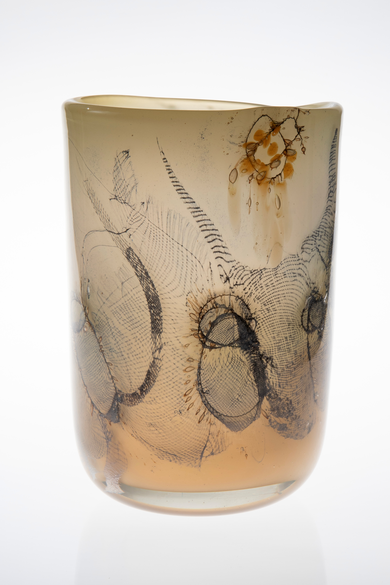 Sylinderformet vase i halvgjennomskinnelig glass. Ujevn munning. Grågrønt underfang som er dekorert med innlagte metalltråder samt partier med finmasket blålig netting. Tidvis brune spetter samt luftbobler i glassmassen. Puntemerke under vasens bunn.
