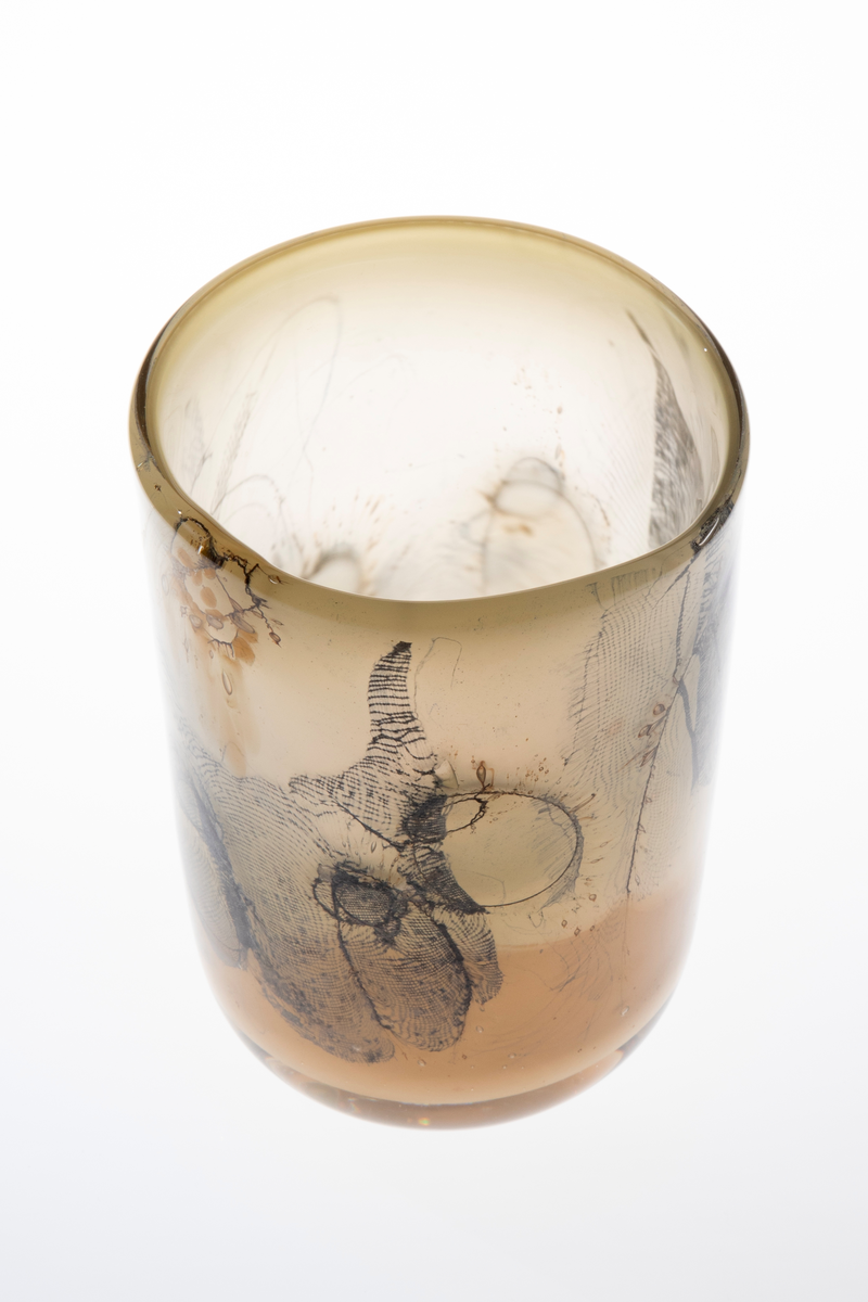 Sylinderformet vase i halvgjennomskinnelig glass. Ujevn munning. Grågrønt underfang som er dekorert med innlagte metalltråder samt partier med finmasket blålig netting. Tidvis brune spetter samt luftbobler i glassmassen. Puntemerke under vasens bunn.