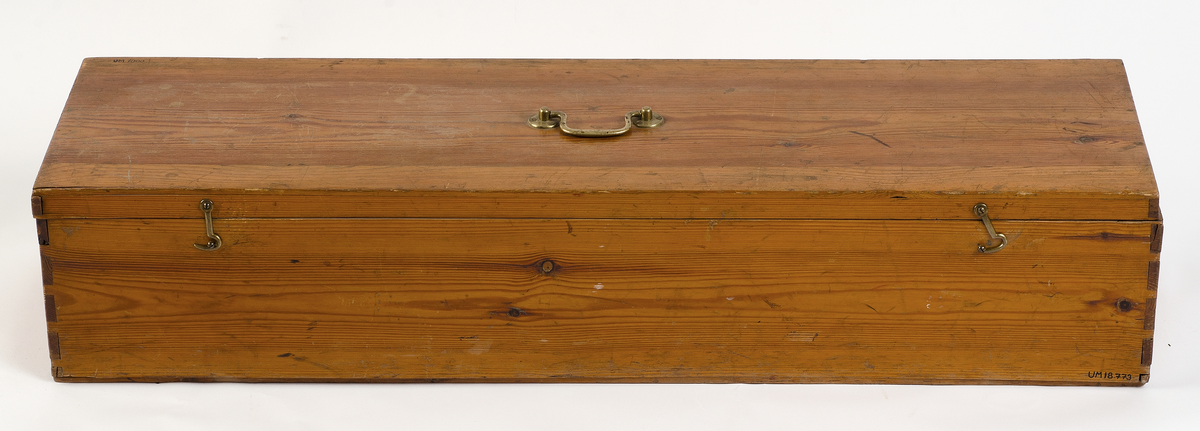 Förvaringslåda för nyckelharpa. Tillverkad av furu med zinkade hörn. Bärhandtag av gulmetall och låskläppar av gulmetall. Inne i lådan ett stöd för harpan klätt med blå filt. Påklistrad etikett med ägarens namn: Knut Håkansson.