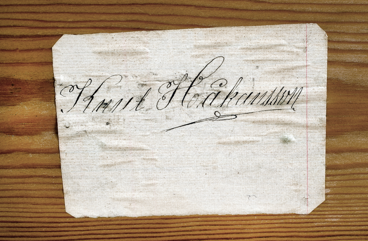 Förvaringslåda för nyckelharpa. Tillverkad av furu med zinkade hörn. Bärhandtag av gulmetall och låskläppar av gulmetall. Inne i lådan ett stöd för harpan klätt med blå filt. Påklistrad etikett med ägarens namn: Knut Håkansson.