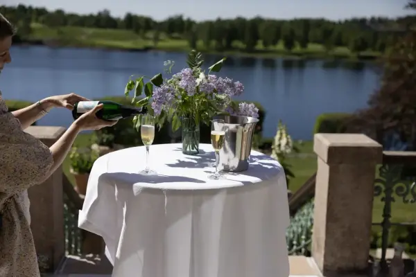 En kvinne sjenker i to glass Champagne. Bogstadvannet i bakgrunnen. 