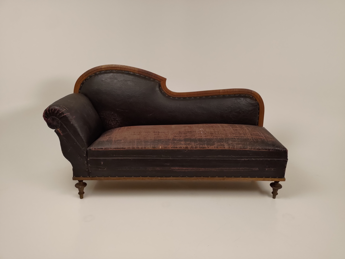 Rektangulær sofa med svungen rygg og opphøyet endestykke (Chaiselongue). Sofaen er trukket med immitert lær (bemalt bomullsstoff). Setet kan løftes opp og trekkes ut, slik at sofaen blir til en sovesofa. Stripet bolstermadrass under setet, utfellbare bein i metall. 
Stoffet (immitert lær) er naglet fast til treverket.
