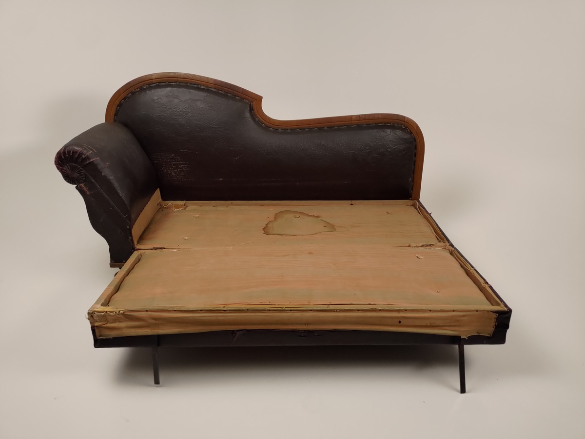 Rektangulær sofa med svungen rygg og opphøyet endestykke (Chaiselongue). Sofaen er trukket med immitert lær (bemalt bomullsstoff). Setet kan løftes opp og trekkes ut, slik at sofaen blir til en sovesofa. Stripet bolstermadrass under setet, utfellbare bein i metall. 
Stoffet (immitert lær) er naglet fast til treverket.