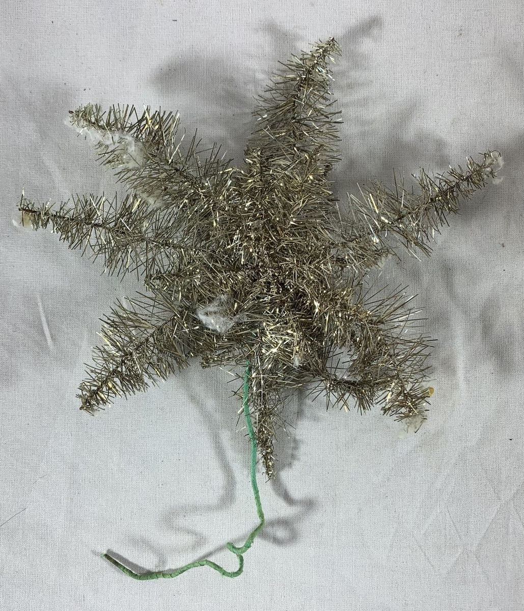 Fem julepyntede stjerner, sannsynligvis beregnet for plassering på toppen av et juletre. Hver stjerne er formet av metalltråd innpakket i sølvfarget glitterdekor, med noen som har små røde kuler som ekstra pynt. Glitteret gir en strålende og festlig effekt, selv om noen av stjernene har tegn til slitasje med deler av glitteret som er borte, og stjerneformene er noe deformert. 

