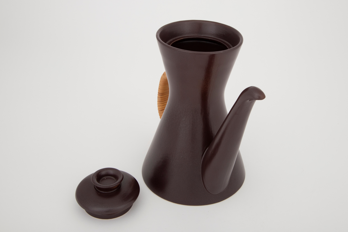 Kaffekanne med lokk i glasert plate- og ovnsfast steingods (novarlitt). Kannen har timeglassform, lang tut og peddigomviklet hank. Mørk sjokoladebrun farge med matt glasur. Bunnen er uglasert.
