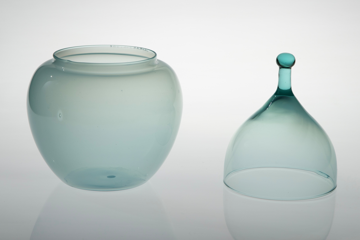 Kuleformet krukke i turkisfarget glass. Kuppelformet lokk som smalner i en lokknapp med kule på toppen. På øvre del av korpus og lokk blir det transparante glasset gradvis halvgjennomskinnelig.