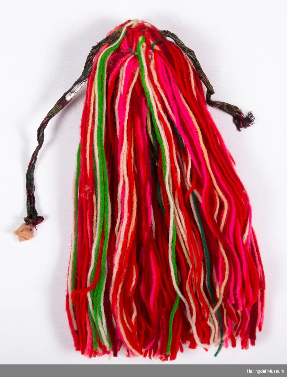 a) Jentepannelin av papp, sylkjety, bolu, kårilsteinar, bomullsty, ullgarn, sydd.
b) Nakkeskuve av flanillsgarn i raudt, mørk raudt, lys raudt, kvitt, lys gult, og grønt.