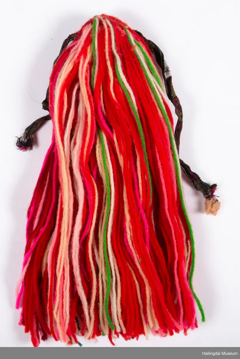 a) Jentepannelin av papp, sylkjety, bolu, kårilsteinar, bomullsty, ullgarn, sydd.
b) Nakkeskuve av flanillsgarn i raudt, mørk raudt, lys raudt, kvitt, lys gult, og grønt.