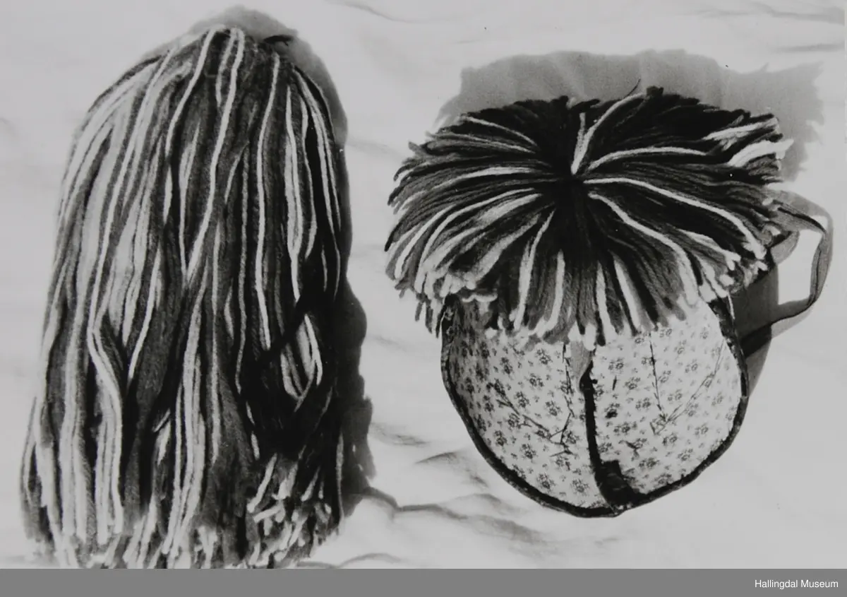 a) Jentepannelin av papp, sylkjety, bolu, kårilsteinar, bomullsty, ullgarn, sydd.
b) Nakkeskuve av flanillsgarn i raudt, mørk raudt, lys raudt, kvitt, lys gult, og grønt.