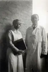 En sjuksköterska och en läkare står vid en tegelvägg utanför