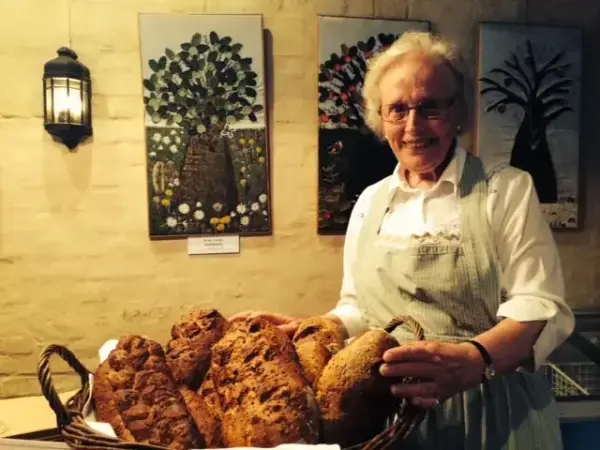 En kvinne står foran en kurv med nybakte brød. 