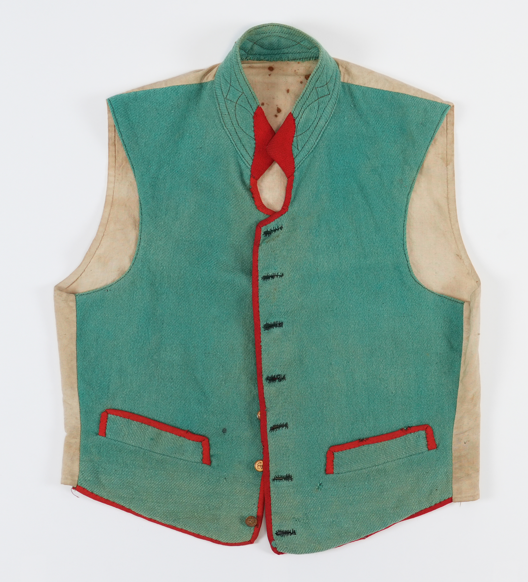 Vest med høg dobbellagd krage, med brune stikningar. Ein liten rund opning mellom kragen og kneppinga. Enkel knapperad, 7 "matrosknappar", det nederste knappet er litt anneledes fra de andre. Avrunda i framkant. Stikklomme med stolpeklaff på kvar side. Framstykka er fora, same stoffet er brukt som bakstykke. Opning og lommekaffar kanta med raude mohairband.