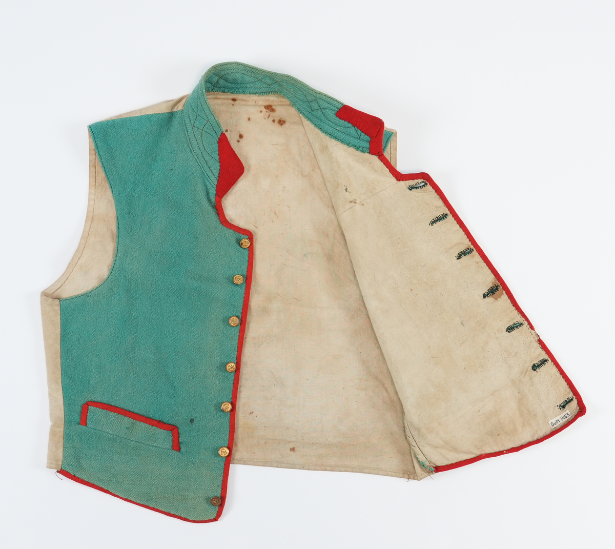 Vest med høg dobbellagd krage, med brune stikningar. Ein liten rund opning mellom kragen og kneppinga. Enkel knapperad, 7 "matrosknappar", det nederste knappet er litt anneledes fra de andre. Avrunda i framkant. Stikklomme med stolpeklaff på kvar side. Framstykka er fora, same stoffet er brukt som bakstykke. Opning og lommekaffar kanta med raude mohairband.