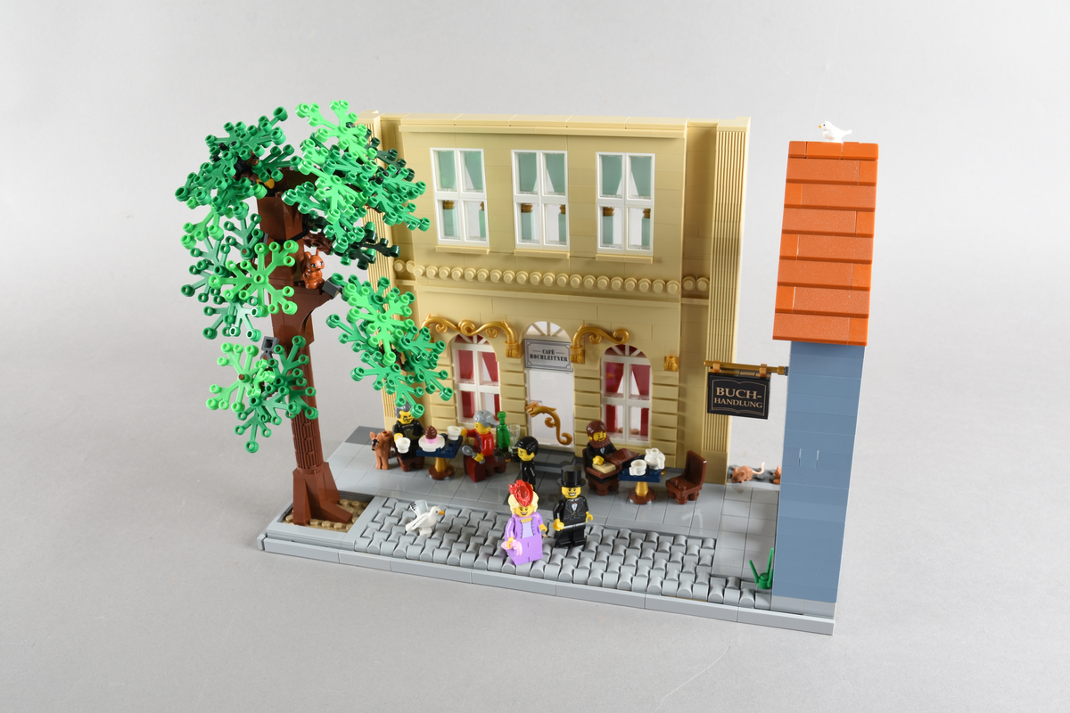 Tablået er bygget av Lego i diverse farger. Scene med syv mennsker stående, gående og sittende utenfor en cafè og bokhandel. Wien 1870, Cafe Hochleitner.