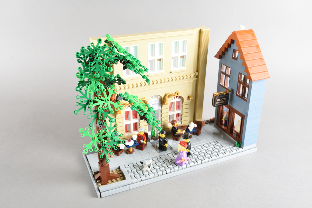 Tablået er bygget av Lego i diverse farger. Scene med syv mennsker stående, gående og sittende utenfor en cafè og bokhandel. Wien 1870, Cafe Hochleitner.