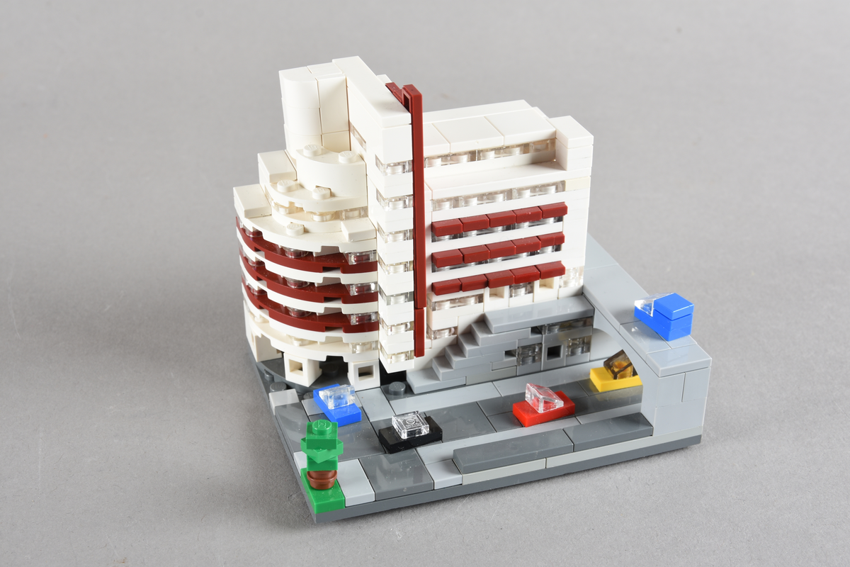Mikrobygg bestående av lego. Tett bygg i hvitt og rødbrunt, med gateplan i grått. Biler på gateplan i rød, gul, sort og blå.