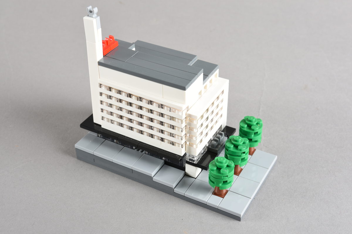 Mikrobygg bestående av lego. Tett bygg i hvitt og grått, med gateplan i grått. Gateplan er grått med brune og grønne trær.