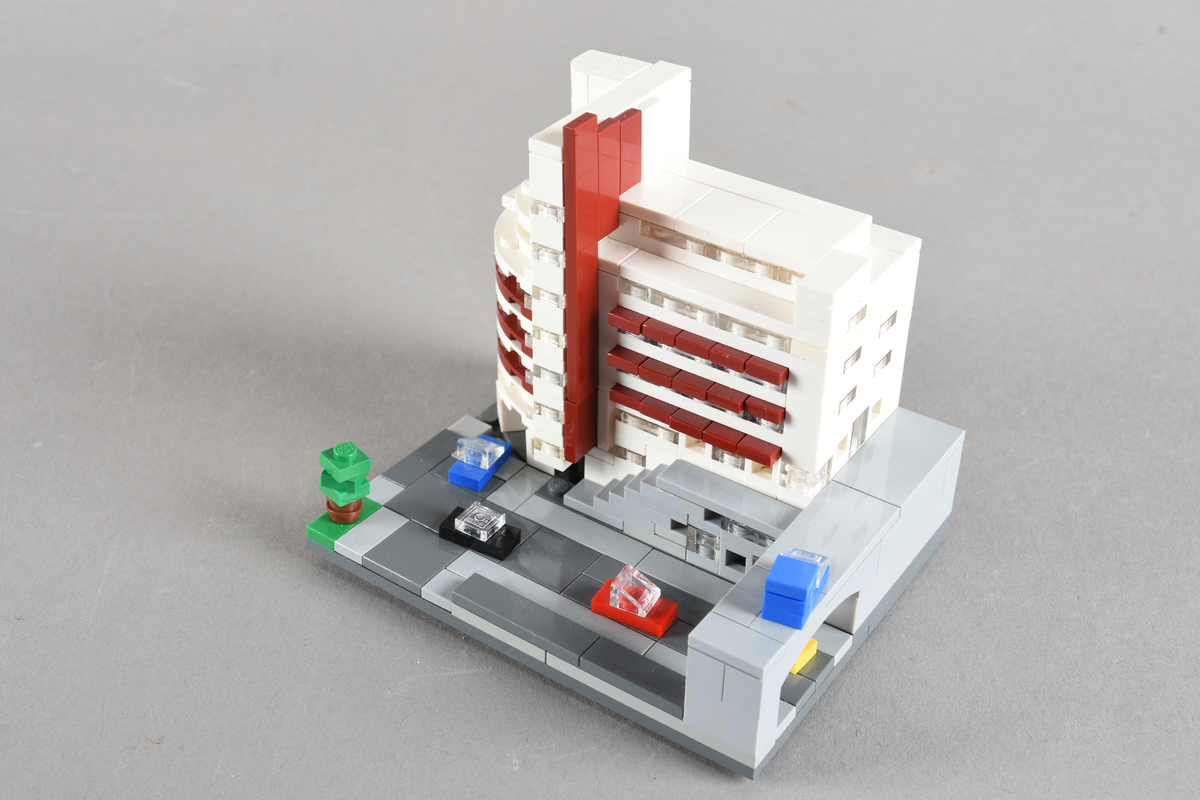 Mikrobygg bestående av lego. Tett bygg i hvitt og rødbrunt, med gateplan i grått. Biler på gateplan i rød, gul, sort og blå.
