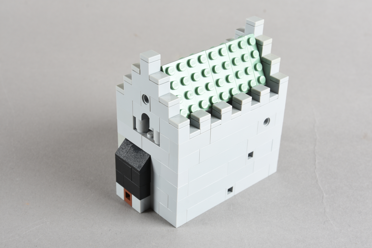 Mikrobygg bestående av lego. Ingen innmat i bygget, kun skallet. Skallet er bygget av grå middels og små legoklosser, med buede åpninger og løst tak. Taket er grønt. Endeveggene har buet åpning høyt på veggen, og en rundt liten åpning med en rød legokloss på innsiden for å imitere et vindu.