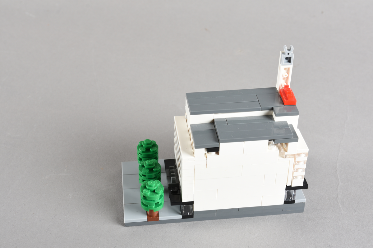 Mikrobygg bestående av lego. Tett bygg i hvitt og grått, med gateplan i grått. Gateplan er grått med brune og grønne trær.