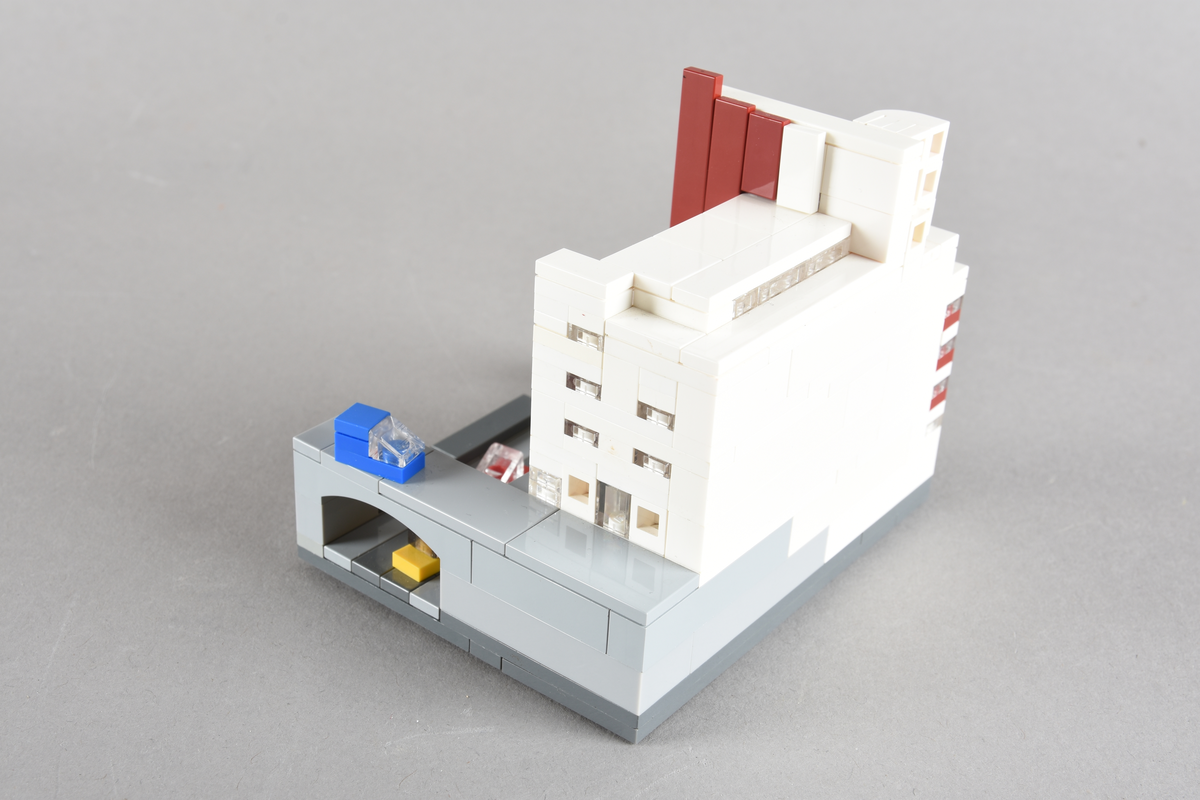 Mikrobygg bestående av lego. Tett bygg i hvitt og rødbrunt, med gateplan i grått. Biler på gateplan i rød, gul, sort og blå.
