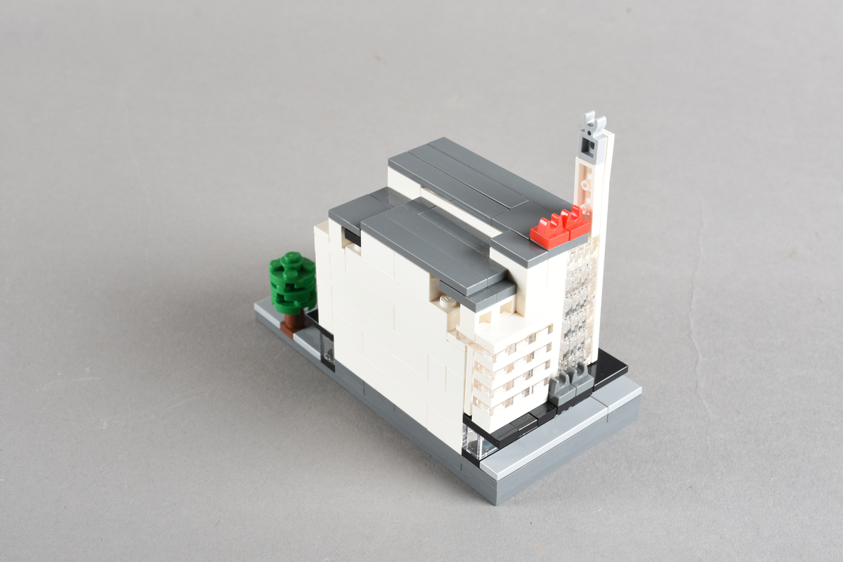 Mikrobygg bestående av lego. Tett bygg i hvitt og grått, med gateplan i grått. Gateplan er grått med brune og grønne trær.