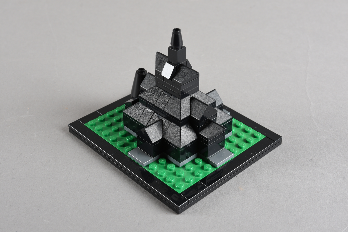 Mikrobygg bestående av lego. Stavkirke av svarte legoklosser, grått underlag og grønt gress/plen.