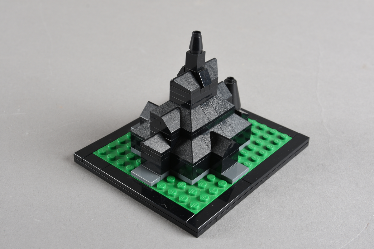 Mikrobygg bestående av lego. Stavkirke av svarte legoklosser, grått underlag og grønt gress/plen.