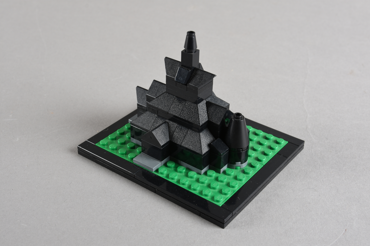 Mikrobygg bestående av lego. Stavkirke av svarte legoklosser, grått underlag og grønt gress/plen.