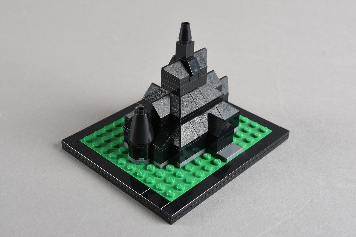 Mikrobygg bestående av lego. Stavkirke av svarte legoklosser, grått underlag og grønt gress/plen.
