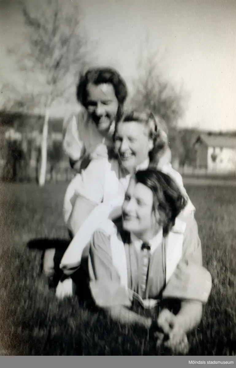 Tre kvinnliga sjukvårdsbiträden halvligger på varandra på en gräsmatta utanför Mölndals sjukhus, 1939 - 1941. Fotot är suddigt. Bilder från fotoalbum, tagna från södra sidan av Länsmansgatan vid Mölndals lasarett/sjukhus 1939 - 1941 på bland annat givarens mor Ester (född Johansson) tillsammans med kollegan/väninnan Aina Englund. De arbetade på den manliga kirurgavdelningen som vårdbiträden/undersköterskor.
Relaterade motiv: 2024_1542 - 1617.