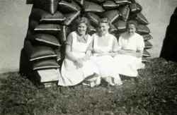 Tre kvinnliga sjukvårdsbiträden sitter på huk i gräset framf