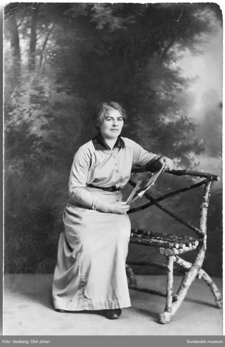 Vykort med ateljéporträtt av en kvinna. På baksidan står: "Grindbacksmon den 6 nov 1915". Ur en samling som tillhört Olivia Larsson, Svartvik.