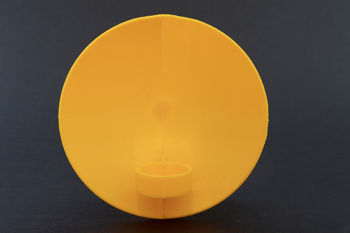 Vegglampe i messing. Rund parabolformet skive med telysholder foran. Rektangulært feste på baksiden med en avstandsplate mellom feste og parabol. Designet tar opp i seg den pre-elektriske lampetypen med reflektorskjerm. 

To 3D-printede protyper i plast. En hvit prototyp for en bordversjon av lampen, som har en rund parabol festet til en høy sylinder. Sylinderen fungerer som både fot og telysholder. Grønt kitt under basen.
 
Gul prototyp for vegglampen. Samme utforming som messinglampen, men har ikke rektangulært feste med avstandsplate på samme måten. Avstandsplaten på prototypen er festet på nedre halvdel av parabolen, og veggfestet er festet direkte på parabolen.